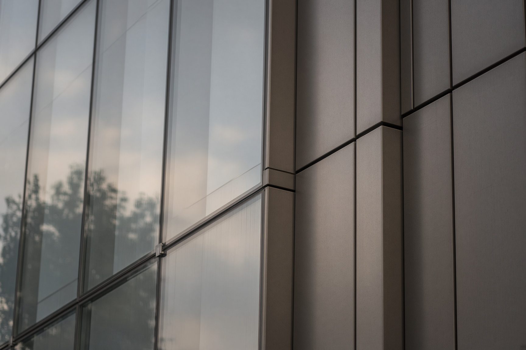 Oblique view of a glass and bronze facade with precise joints and soft sky reflection.