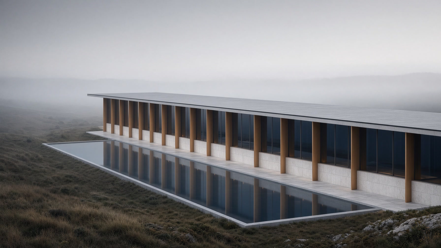A long linear stone-and-glass building under one roof, fog over still water at dawn.
